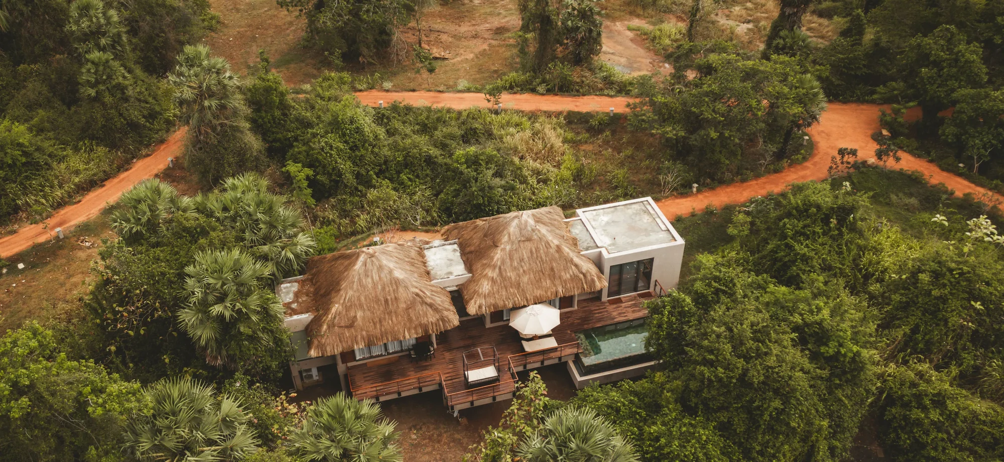 A drone view of one of the Deluxe Villas at Ulagalla, it is encased by verdant foliage and has thatched roofing.