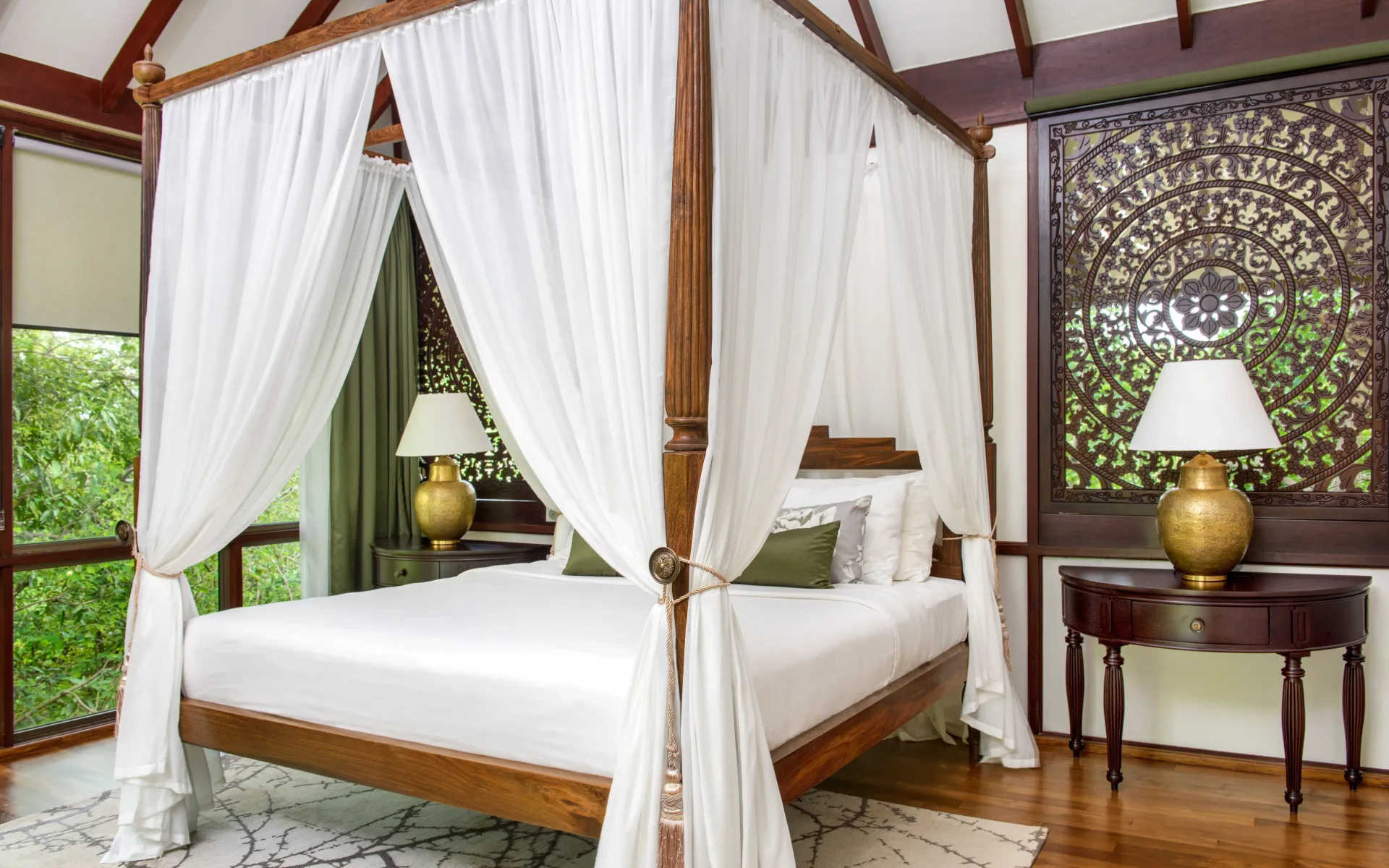 A four-poster bed is surrounded by intricate decor and dressed in soft, white bedding.