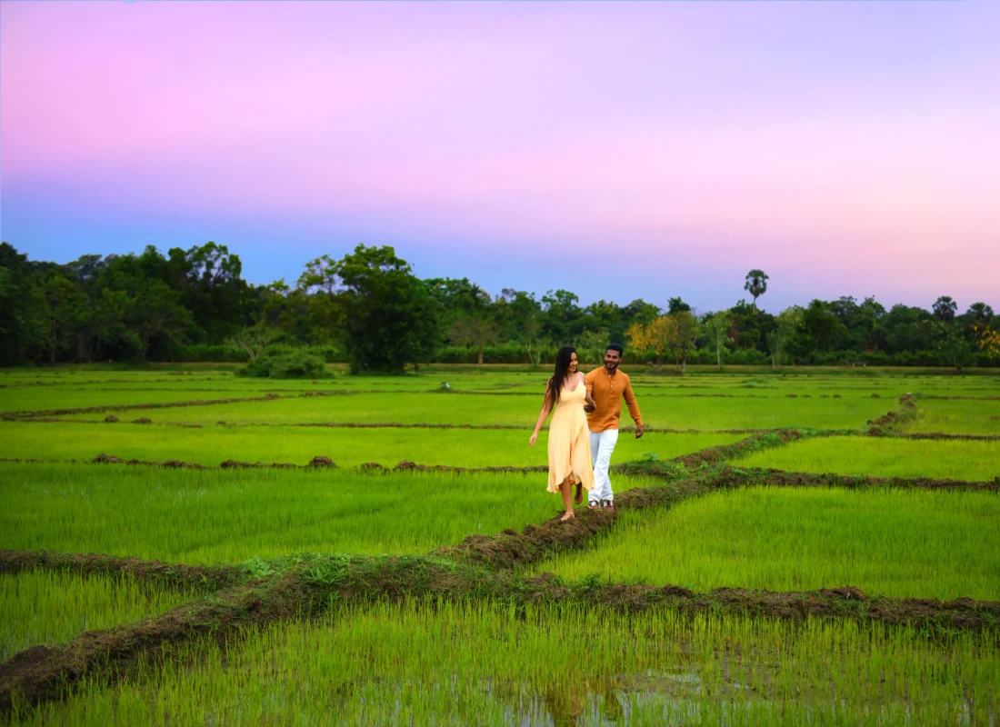 A couple take a bare-foot walk along emerald paddy fields ahead of a lilac sunset.
