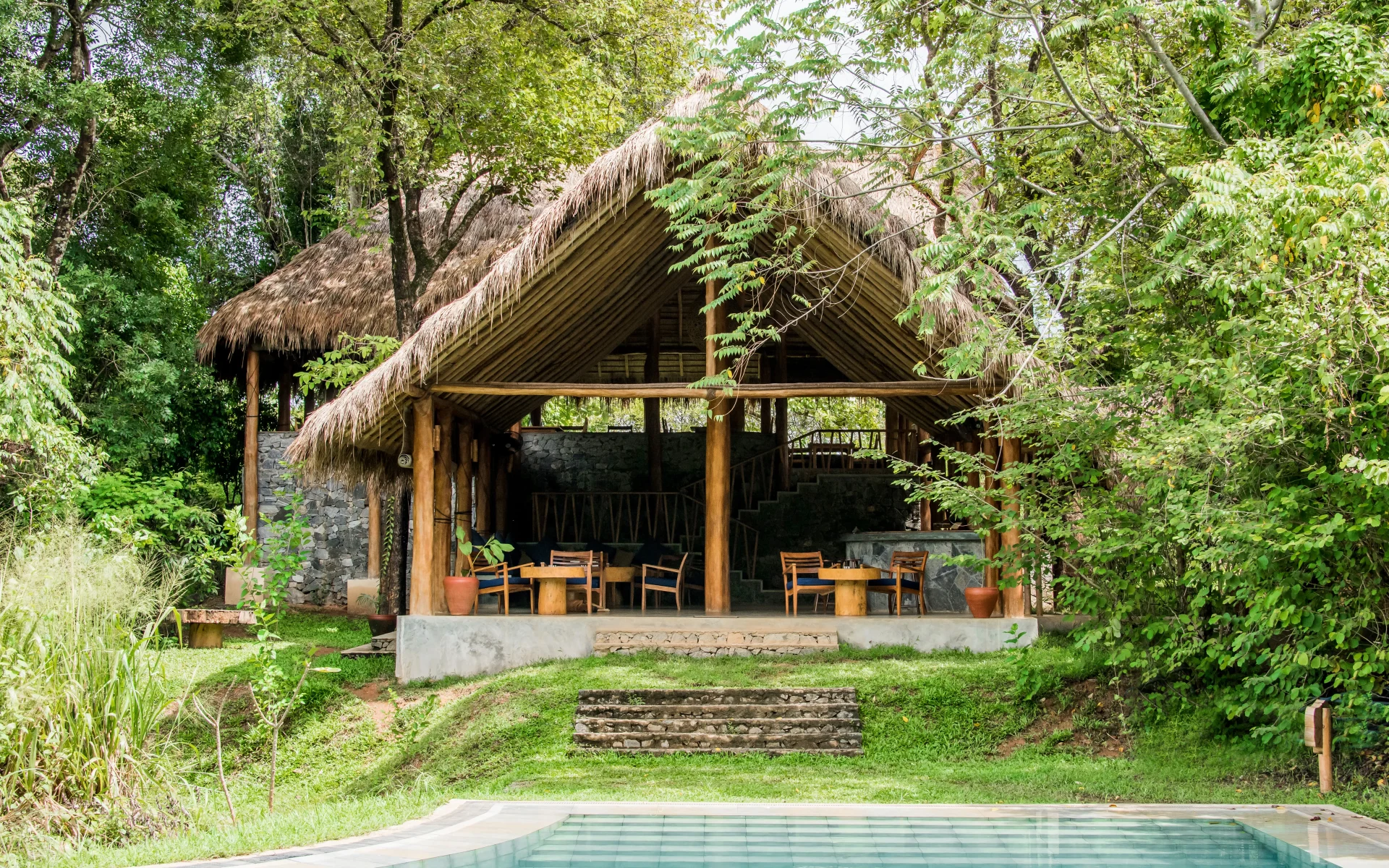 The poolside bar is in a thatched-roof hut. Steps lead down to the outdoor pool, encased by foliage.