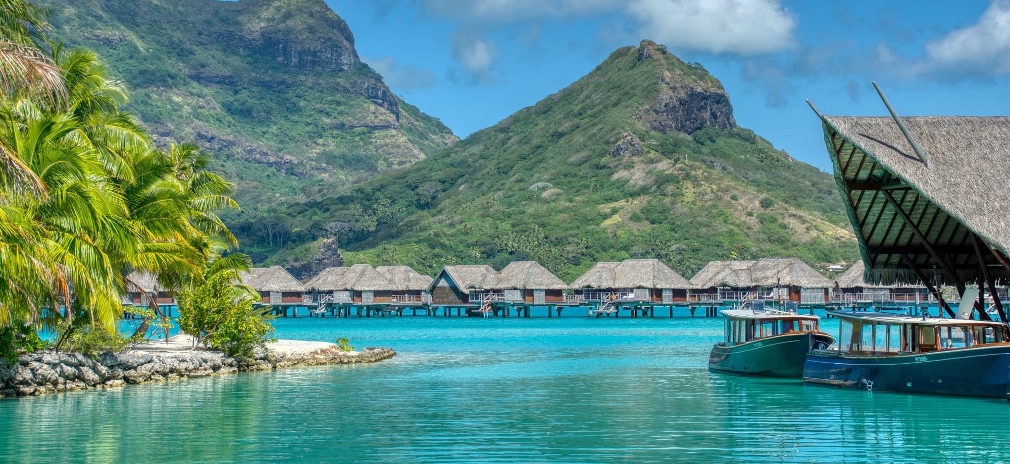 Overwater villas are backed by towering green mountains, palm trees and glistening turquoise waters. 