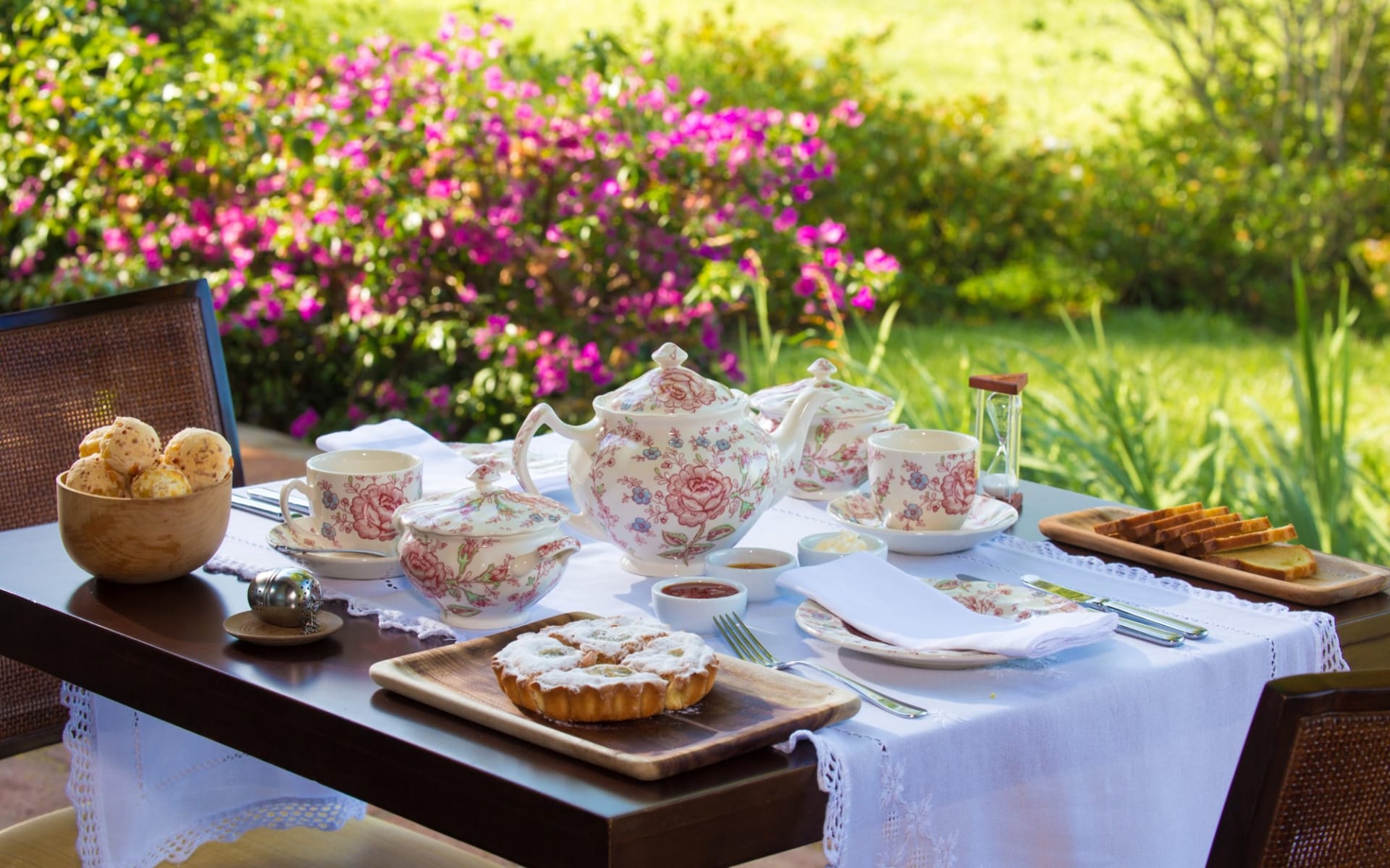 A breakfast table is set up with china cups, teapots and pastries. 