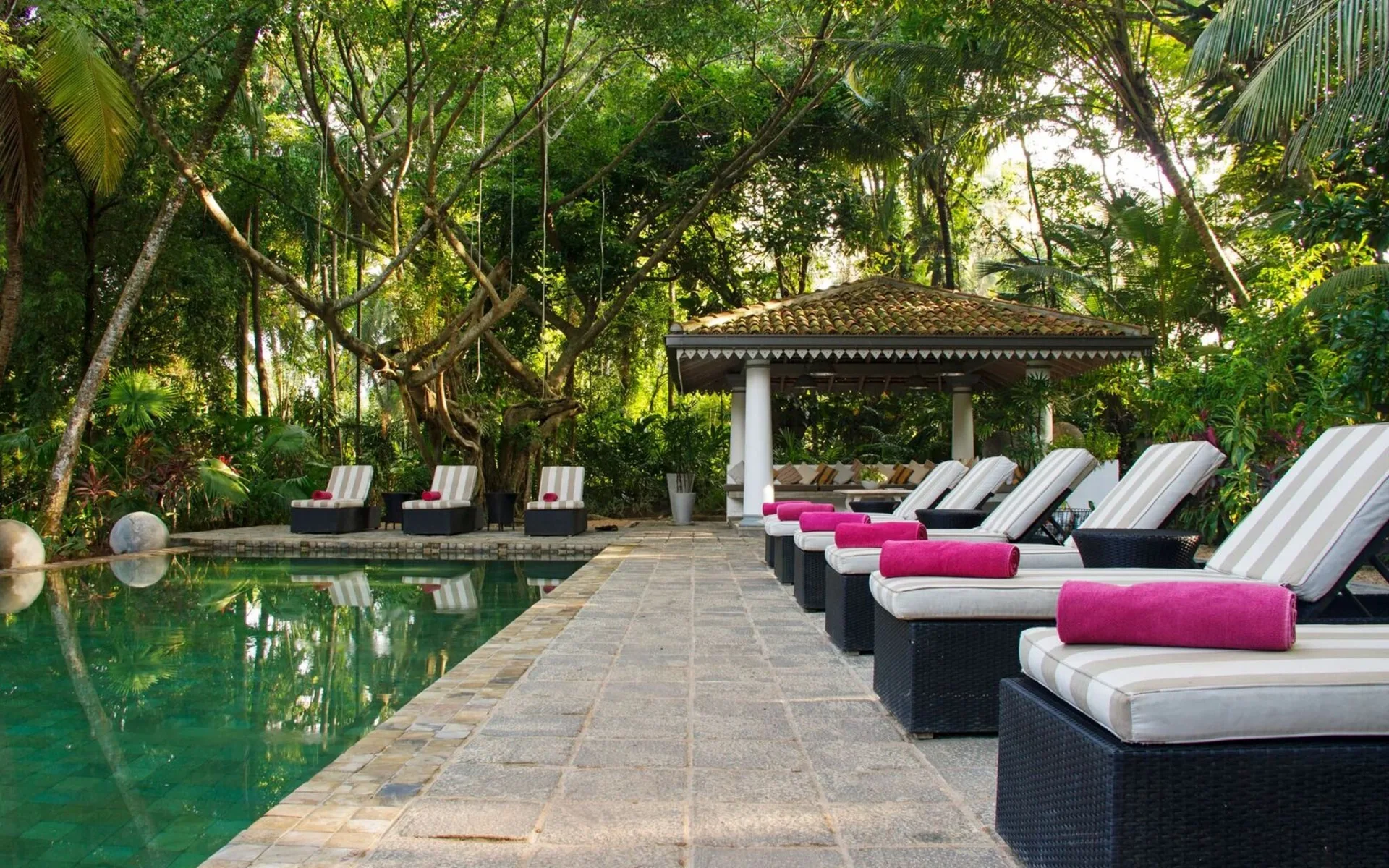 The main swimming pool is surrounded by a stone-paved sun deck with sun loungers that have pink towels placed on them.