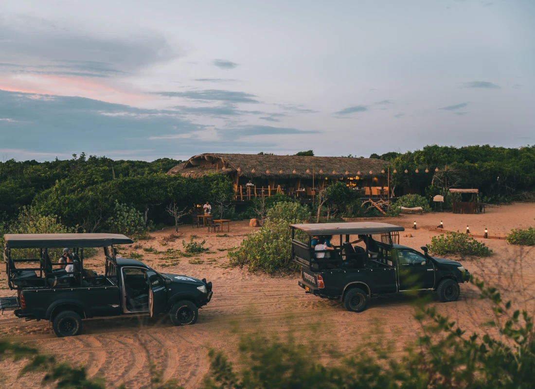 Two safari vehicles are outside the thatched cottage at Chena Huts.