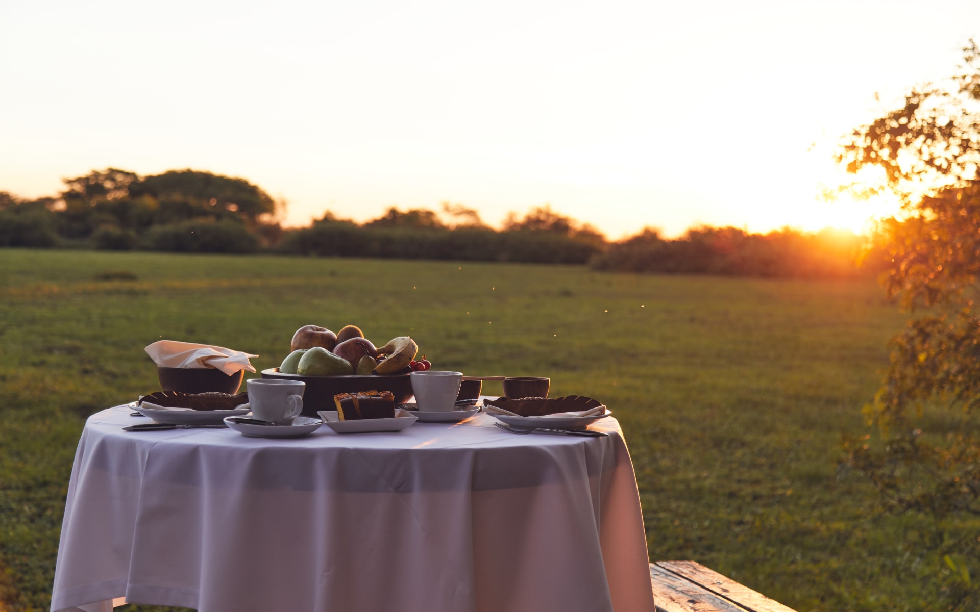 A table with white cloth is laid out in the lawn as the sun is setting. 