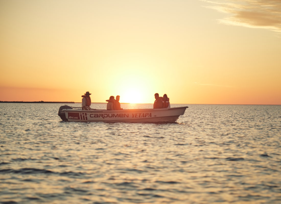 In the ocean is a small motorised boat, with people sitting and watching the sun set on the horizon.