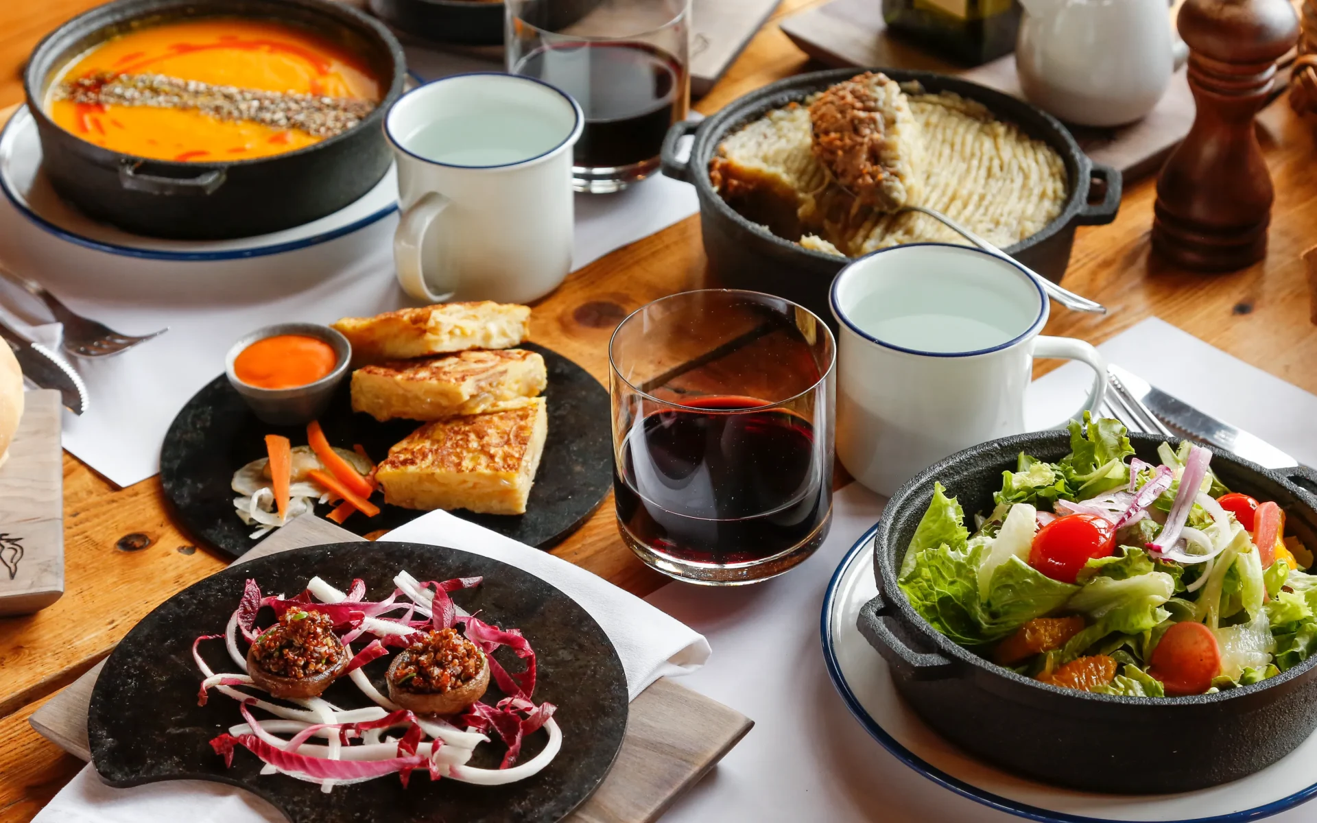 A selection of delicious, colourful dishes are laid out on the table, alongside two glasses of red wine.
