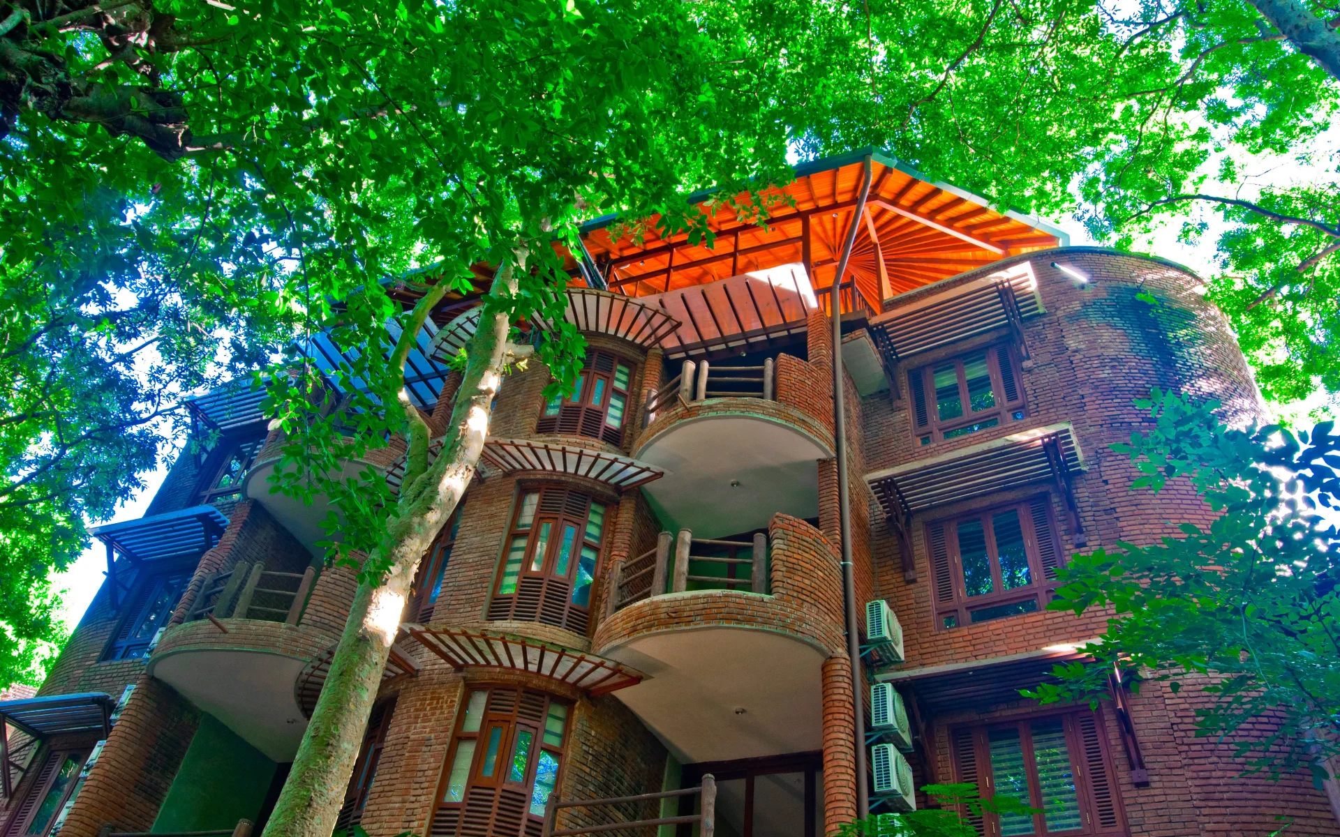 The main building has innovative architecture and is multi-storied, surrounded by tall trees.