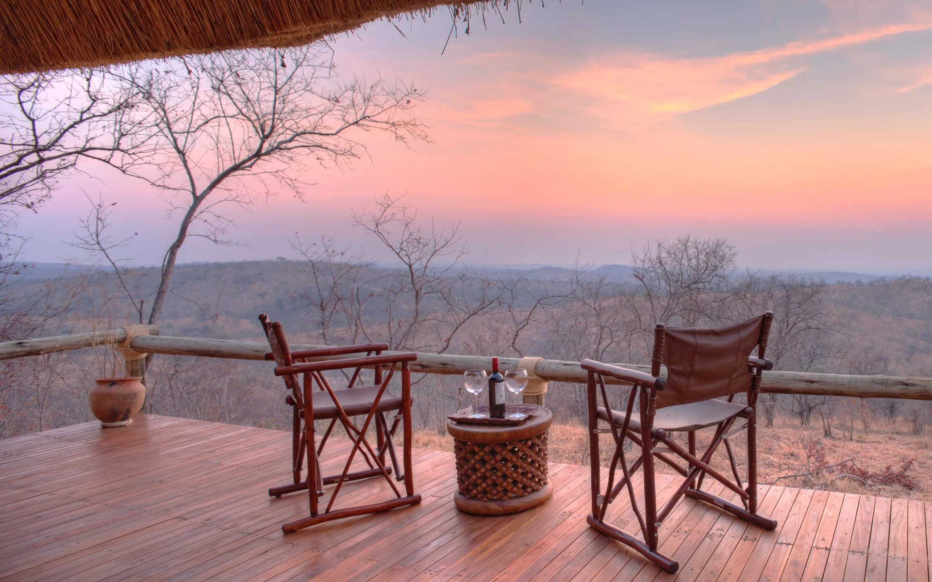 Two camping chairs are set up on the Ikuka Lodge decking, overlooking a beautiful sunset panorama.