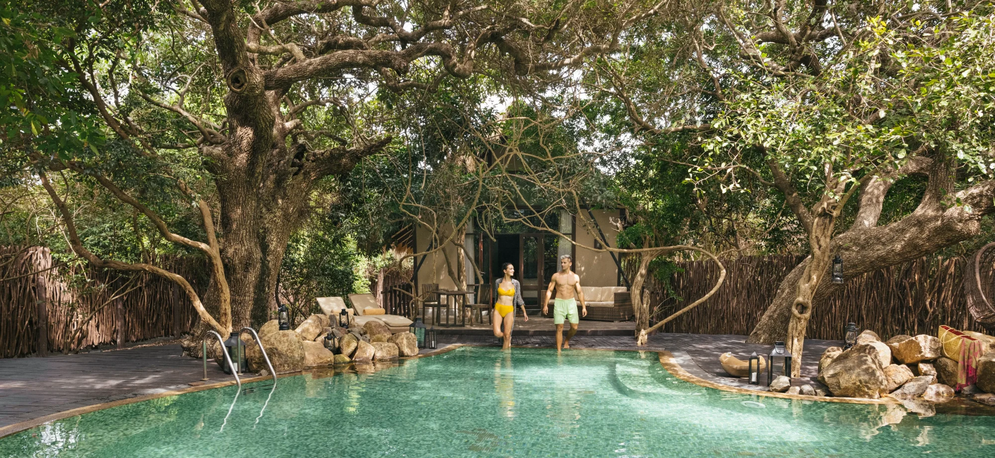 Couple walking into Jungle Beach's outdoor pool, surrounded by lush tropical trees.