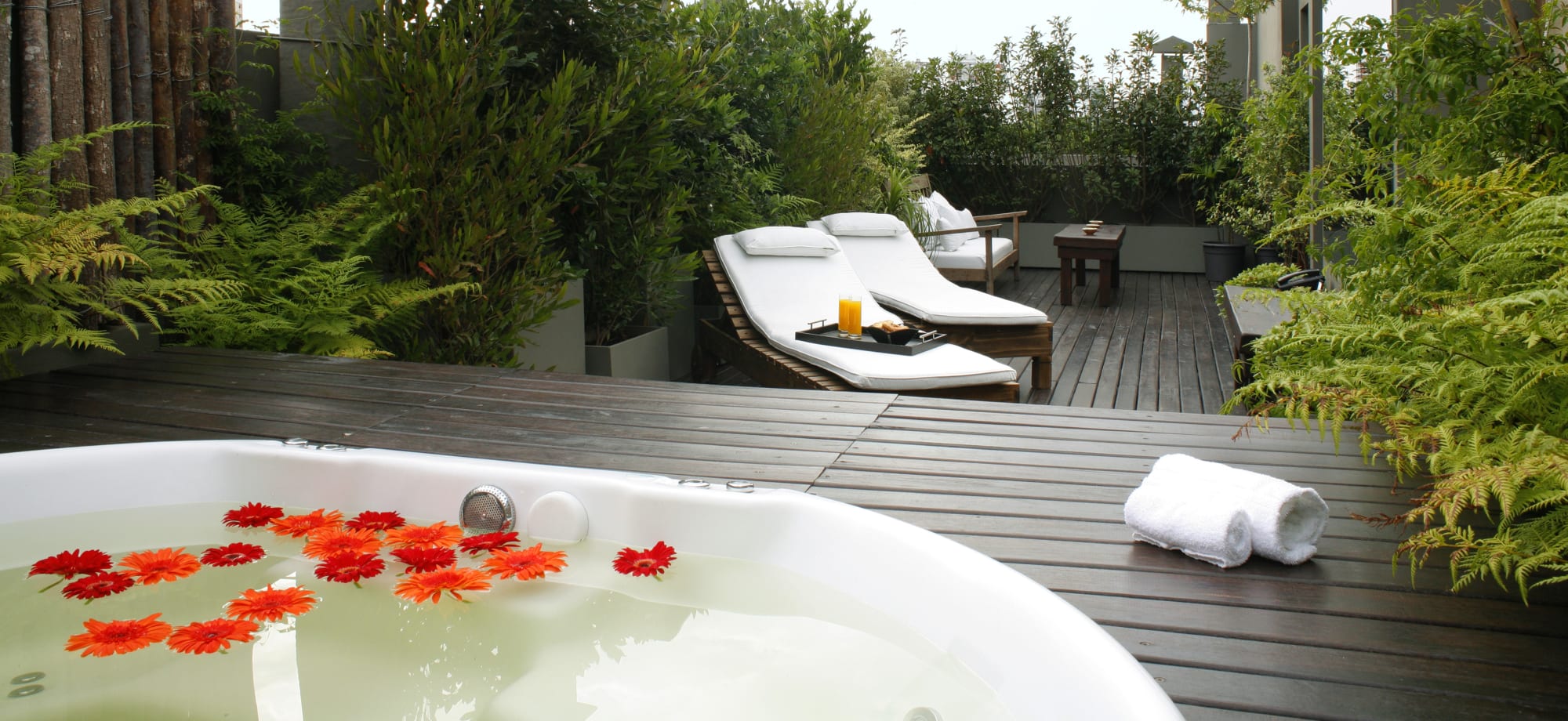 Legado Mitico terrace has a whirlpool bathtub with flowers floating on its surface and deck chairs surrounded by plants. 