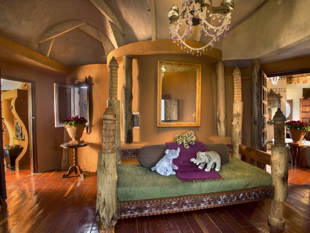 A four-poster bed with elephant teddies and a grand chandelier above