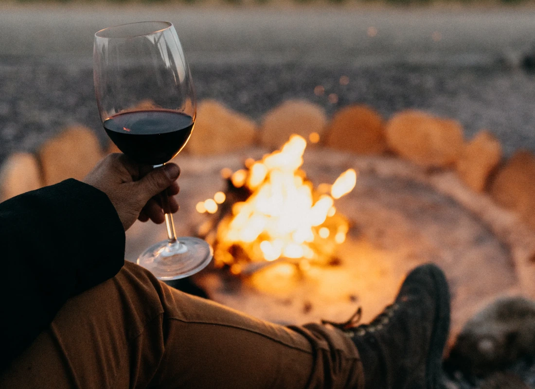 A guest is enjoying a glass of red wine ahead of a warming log fire.