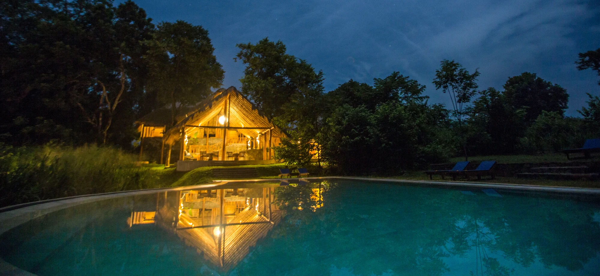 One of the huts at Gal Oya Lodge backs onto the outdoor pool and is lit up with warm lighting during a gentle evening.