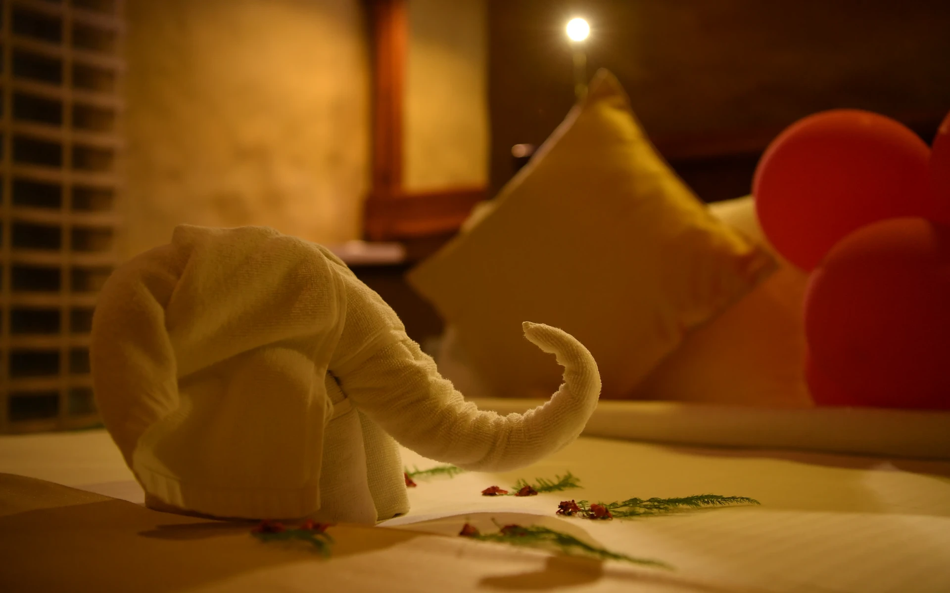 An adorable towel origami elephant sits on  double bed in a warmly-lit room.