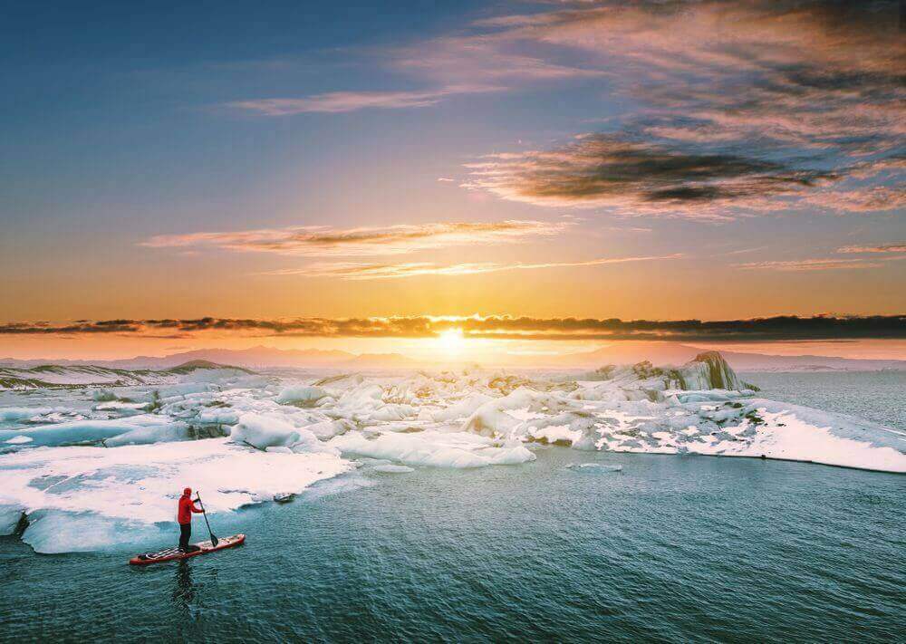 traveller stand up paddleboarding in antarctica at sunrise