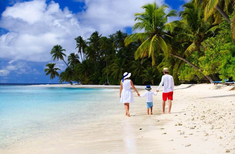family walking along the palm fringed beach in the maldives