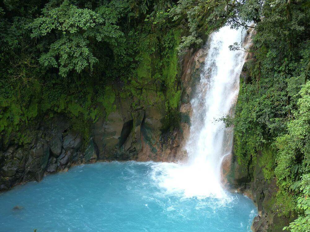 bright blue water surrounded by green jungle of a waterfall in costa rica