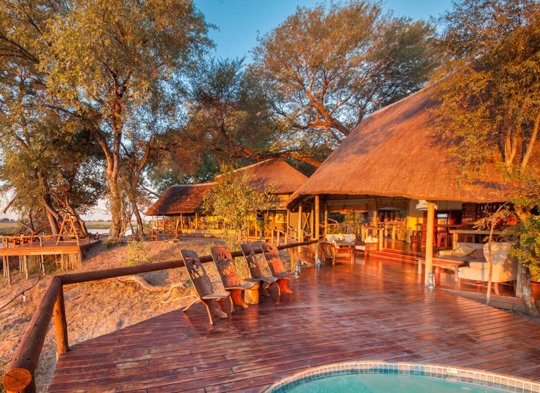 The sun is setting over the camp's thatched roofs and deck with a swimming pool. 