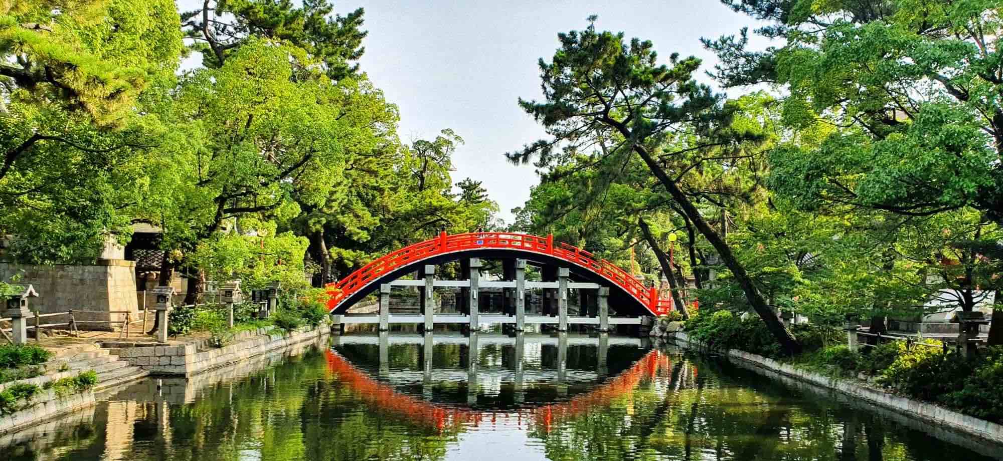 A half-circle red bridge is reflected in a river in Osaka.