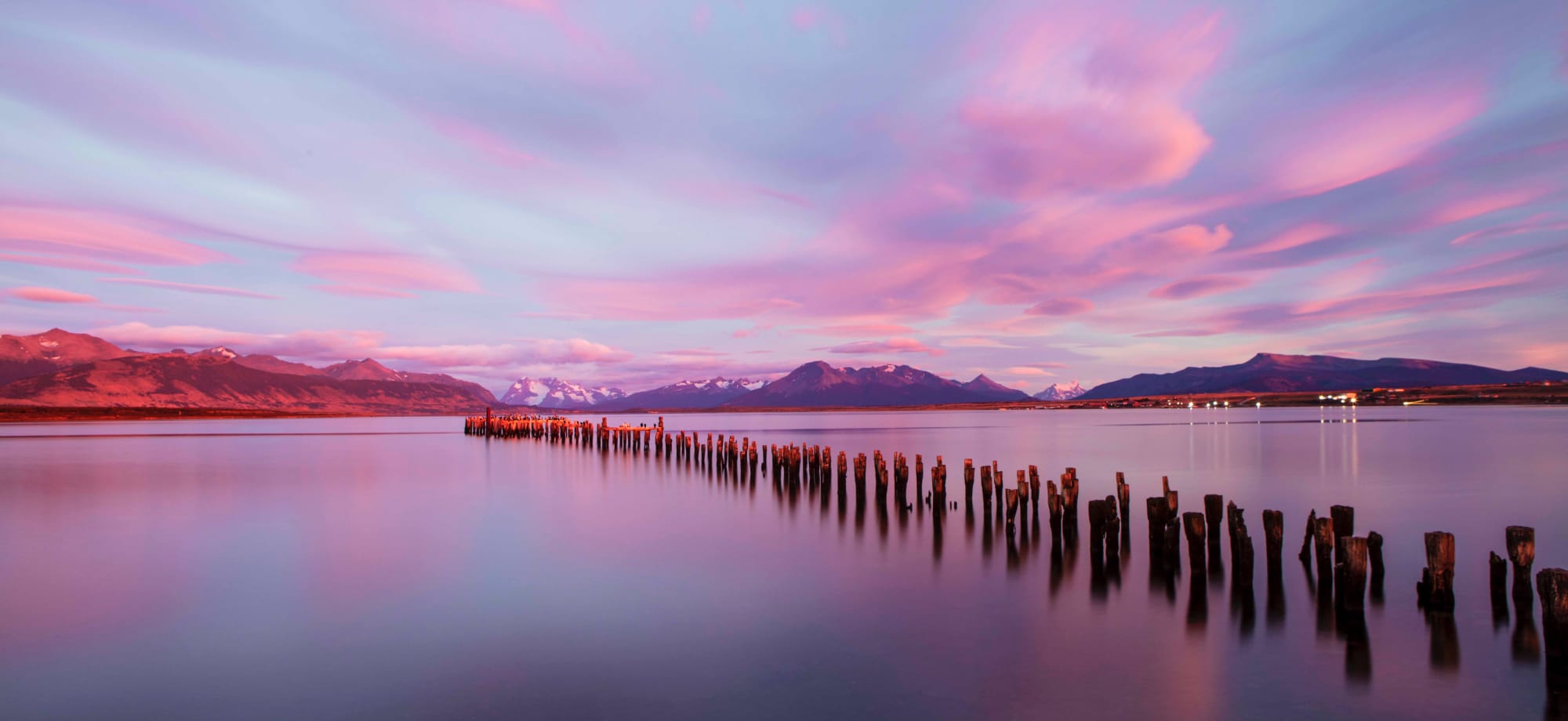 In Chilean Patagonia, the sun is setting over a lake, casting hues of pink, blue and purple over the water. 
