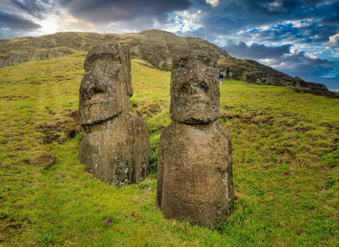 Two statues stand tall on the side of a mountain on Easter Island. 