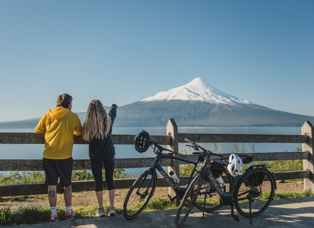 A couple have paused their bike ride to look at the snow-capped mountain and glistening lake.