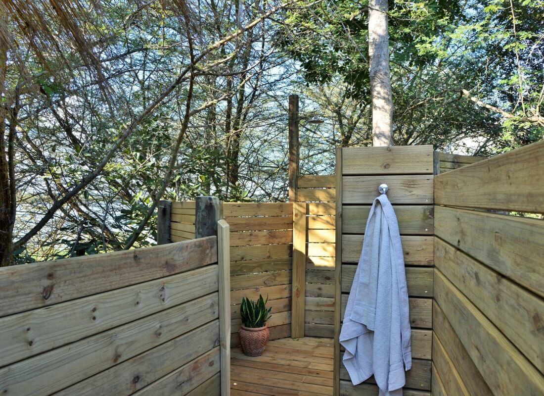 An outdoor shower with potted plants, trees and a hanging towel.