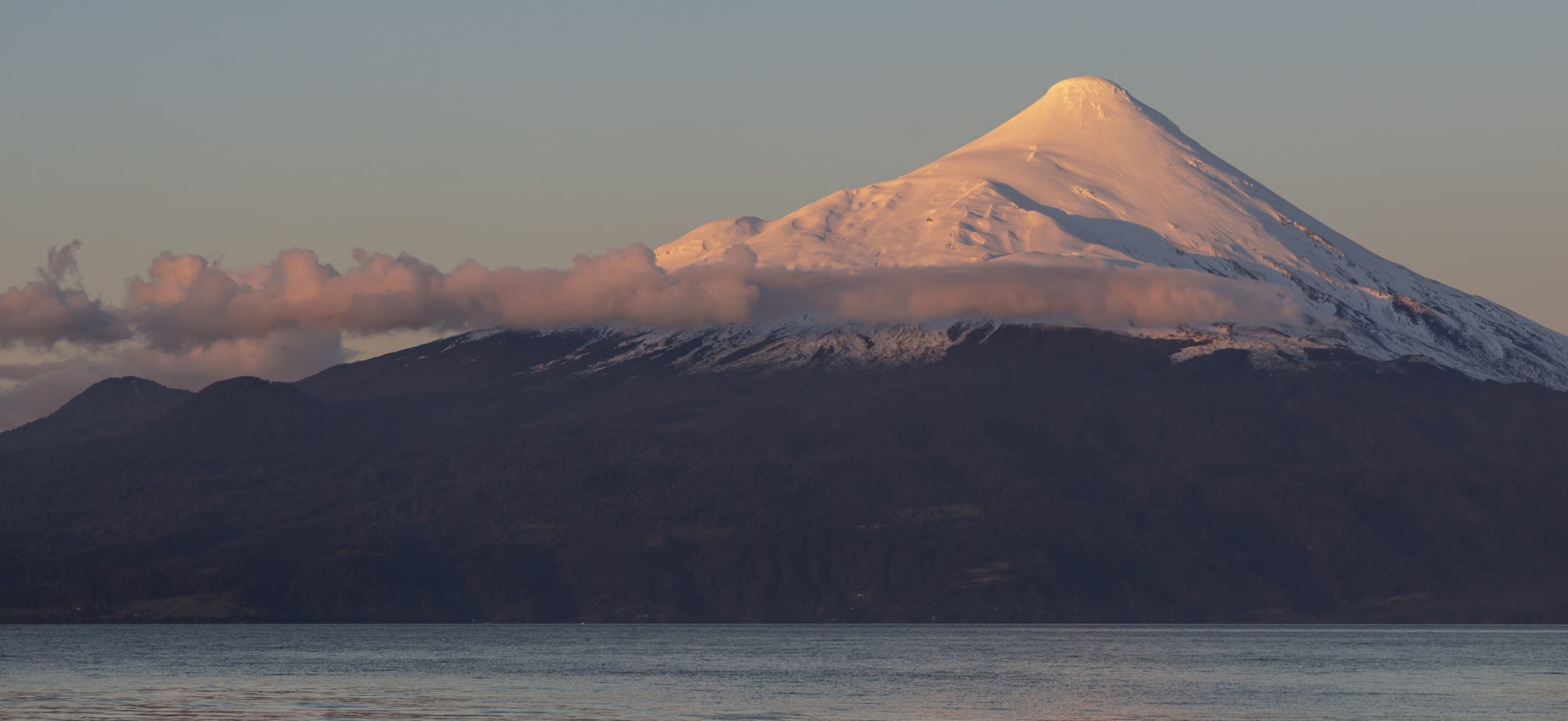 A snow-capped mountain is glowing orange from the sunset. 