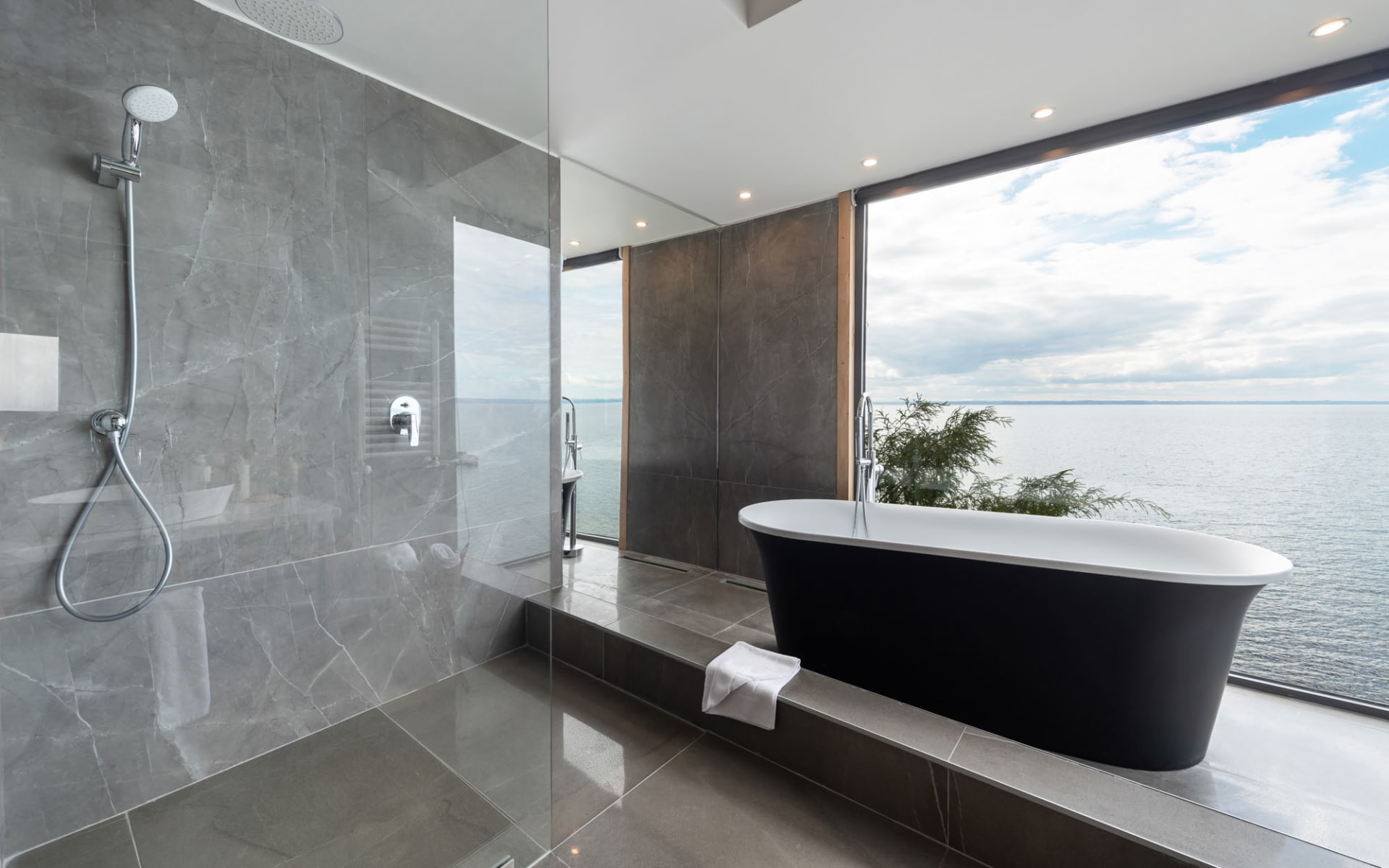 A roll-top bath tub and walk-in rainfall shower fill the bathroom and look out of floor-to-ceiling windows. 