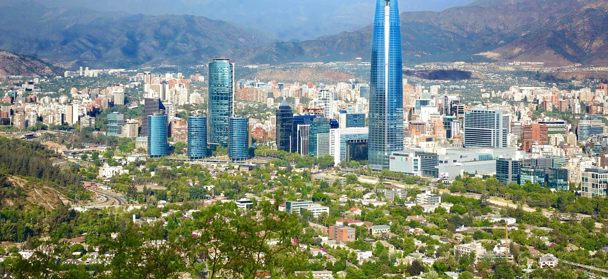 The city of Santiago in Central Chile is surrounded by mountains and interspersed with skyscrapers, clusters of buildings and trees. 
